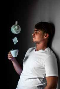 man leaning on wall while holding white ceramic cup